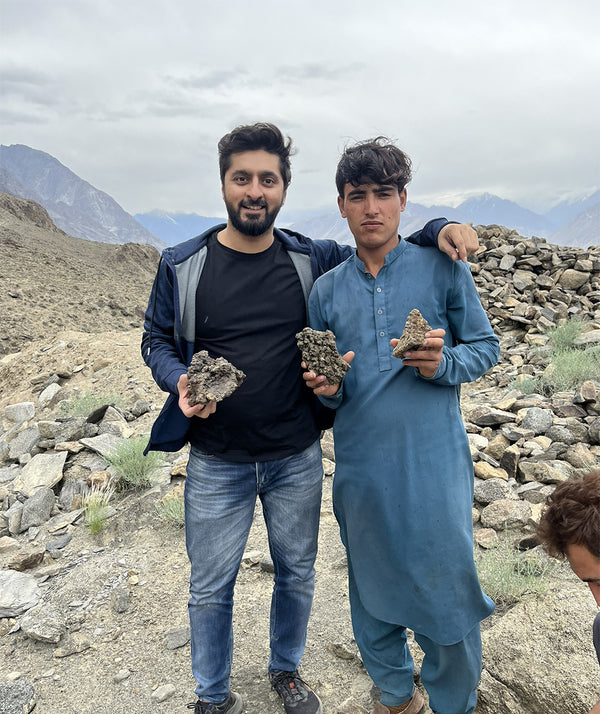 Two men holding shilajit rocks in a mountainous landscape